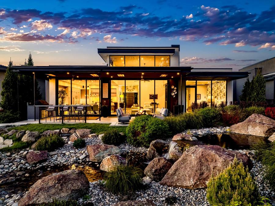 Modern luxury home with a lit glass great room and patio at dusk