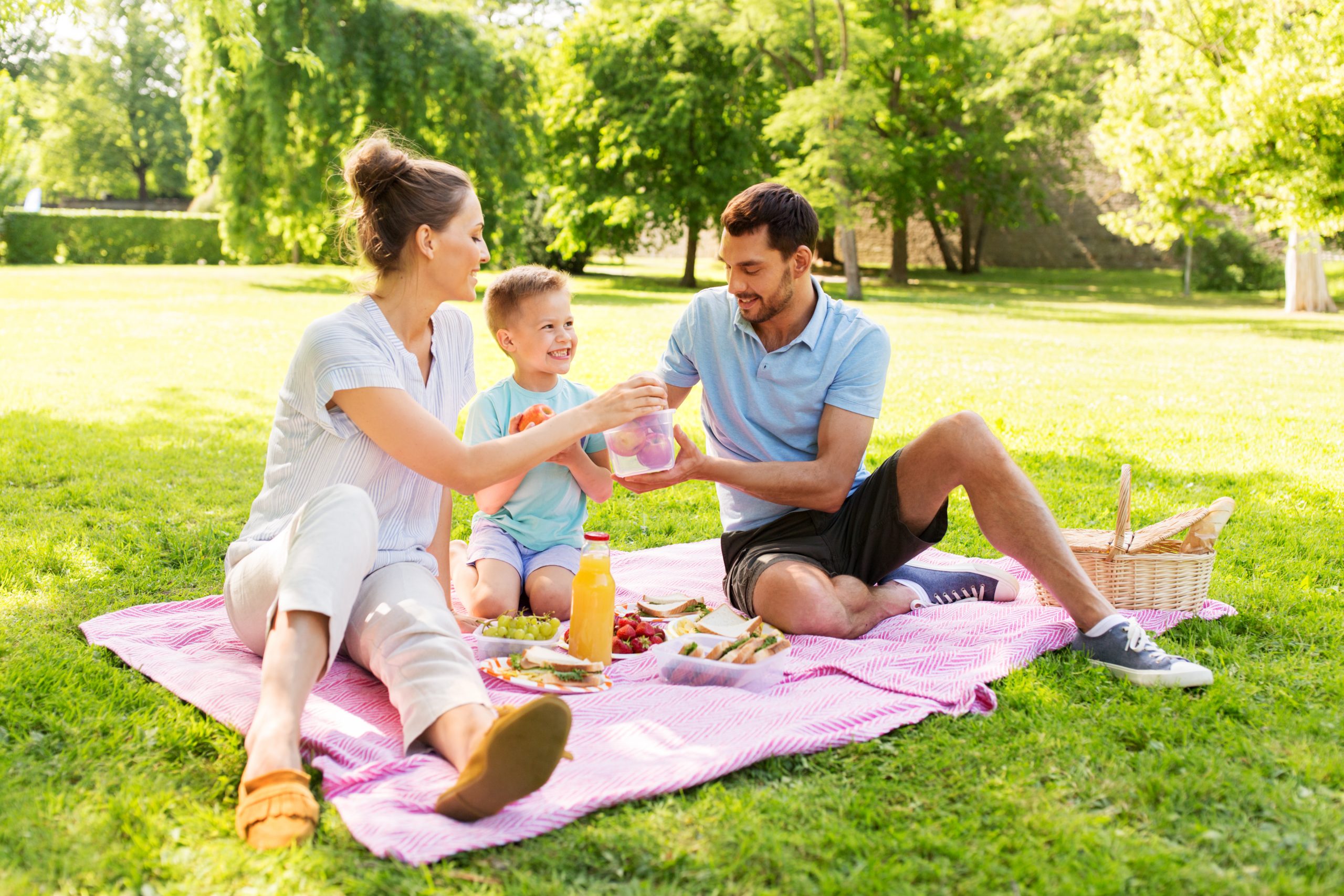 family, leisure and people concept - happy mother, father and little son having picnic at summer park