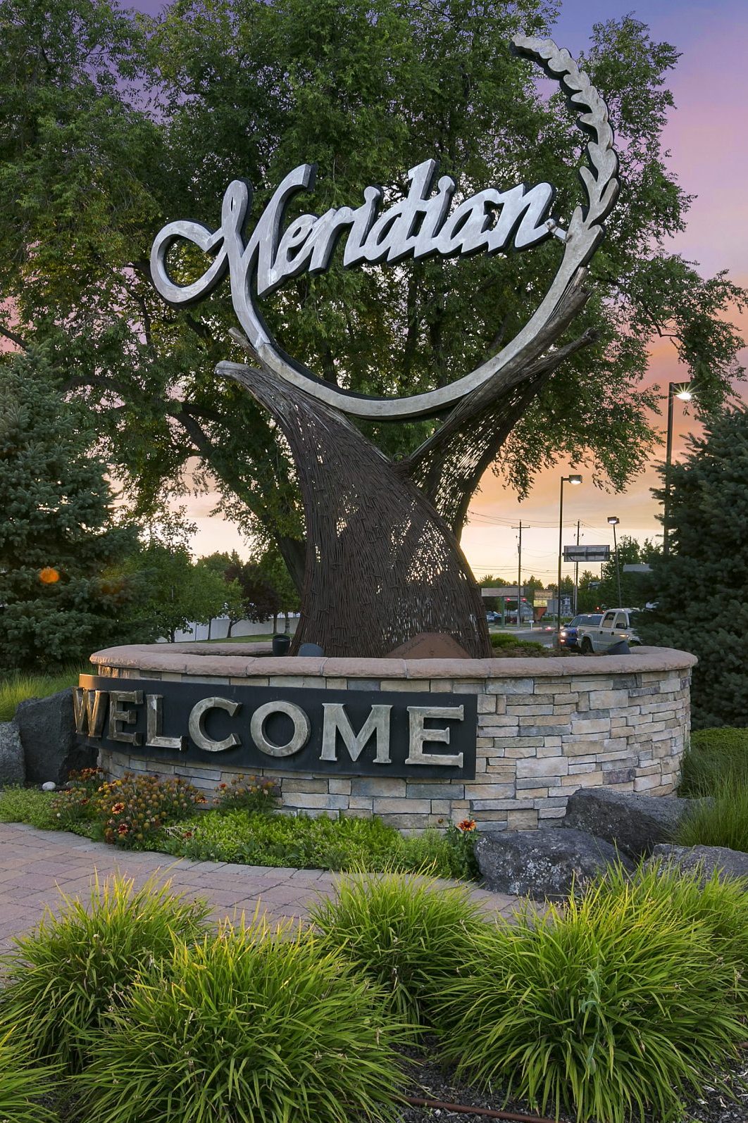 Meridian Idaho Welcome sign at an angle. Large tree behind sign with sunset peeking through