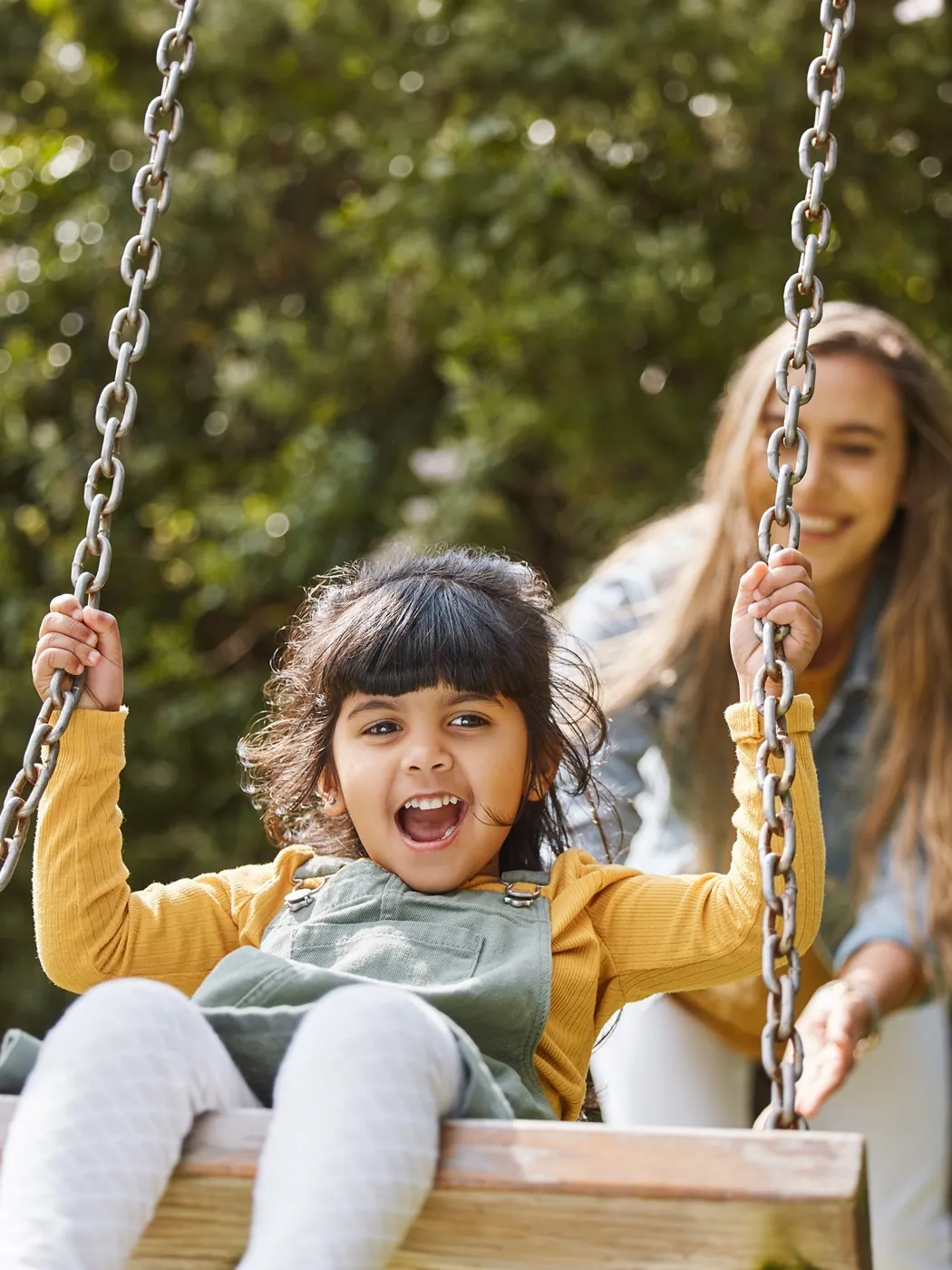 A mother pushing her daughter on a swing
