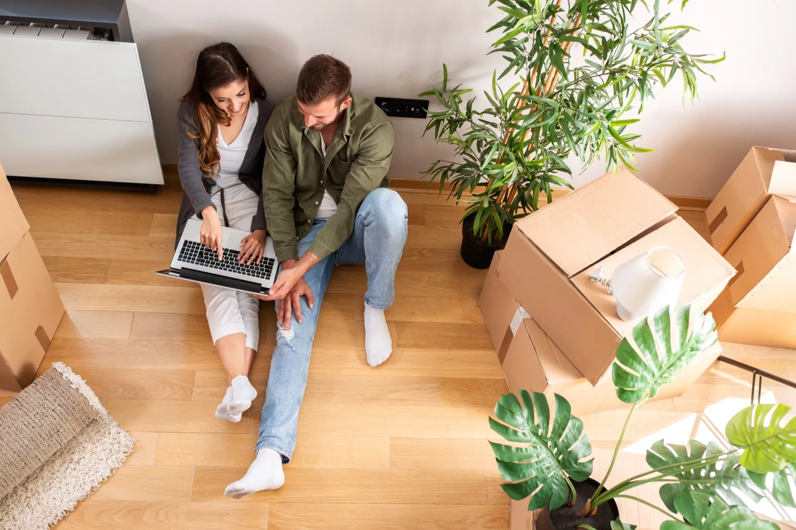 A couple sitting among moving boxes looking up home values on a laptop